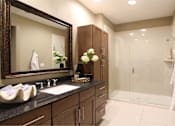 Thumbnail 22 of 42 - Spacious bathroom with built-in shelves, frameless glass walk-in shower, and granite slab vanity top Tuscany Walk Apartments in Houston.