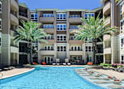 Thumbnail 18 of 42 - Luxury apartments with resort-style pool and palm trees, fountains, lap lane, and pool-side lounge chairs at Tuscany Walk Apartments in Houston