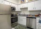 Thumbnail 3 of 42 - Kitchen with white cabinets, stainless steel appliances, and breakfast bar at Woodlake on the Bayou Apartments