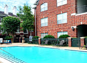 Thumbnail 24 of 36 - Luxury apartments with red brick exteriors, large swimming pool with spacious sundeck, grill, beautiful landscaping, lush landscaping, chaste trees, and pool-side lounge seating at Tuscany Apartments in Houston.
