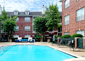 Thumbnail 12 of 36 - Luxury apartments with red brick exteriors, large swimming pool with spacious sundeck, grill, beautiful landscaping, lush landscaping, chaste trees, and pool-side lounge seating at Tuscany Apartments in Houston.
