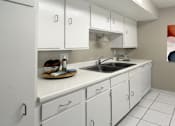 Thumbnail 1 of 10 - Bright white kitchen with gray wall color, white kitchen cabinets, lots of cabinet space, lots of counter space, and porcelain tile floors at The Inverness Apartments in La Vista, Nebraska
