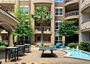 Thumbnail 19 of 36 - Luxury apartments with palm trees, spacious sundeck with poolside lounge chairs, grilling station, ping-pong table, and fountains at Villa Piana Apartments in Dallas