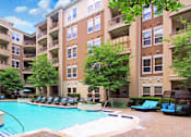 Thumbnail 27 of 36 - Luxury apartments with resort-style pool, palm trees, spacious sundeck with poolside lounge chairs, grilling station, fountains, and fitness center at Villa Piana Apartments in Dallas