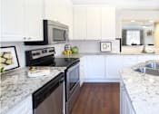 Thumbnail 3 of 26 - Spacious kitchen with island, granite countertops, white cabinets, smooth glass top stove, spacious pantries, breakfast bar and stainless-steel appliances at Tuscany Villas in Houston.