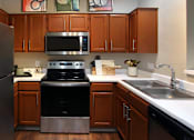 Thumbnail 2 of 36 - Luxury kitchen with wood plank floors, stainless steel appliances, honey brown cabinets, and white countertops at Lenox Village Apartments