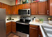 Thumbnail 24 of 36 - Luxury kitchen with wood plank floors, stainless steel appliances, honey brown cabinets, and white countertops at Lenox Village Apartments