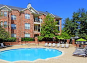 Thumbnail 56 of 73 - Gated apartment community with brick exteriors, lush landscaping, two swimming pools with poolside lounge chairs, spa, and sauna at The Saxony Apartments