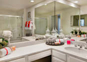 Thumbnail 15 of 36 - Spacious bathroom with oval soaking tub with glass enclosure, cultured marble vanity, glass shower, and built-in vanity at Tuscany Apartments in Houston.