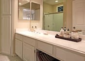 Thumbnail 31 of 42 - Luxury apartments with white cabinets, linen closet, extra cabinet space, cultured marble vanity, built-in vanity, roman tub with glass door and shower, and porcelain tiled floor at The Biltmore Apartments in Omaha, Nebraska