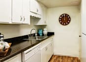 Thumbnail 4 of 19 - Apartments near the Galleria with bright white kitchens, black countertops, and wood plank flooring at Plantation apartments in Houston.