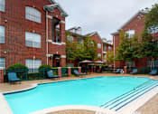 Thumbnail 36 of 36 - Luxury apartments with red brick exteriors, large swimming pool with spacious sundeck, grill, beautiful landscaping, lush landscaping, chaste trees, and pool-side lounge seating at Tuscany Apartments in Houston.