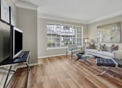 Thumbnail 11 of 40 - Spacious living room with wood laminate flooring, oversized window, gray painted walls, and decorative crown molding at Village on the Parkway Apartments in Houston Texas
