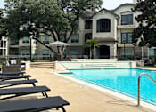 Thumbnail 1 of 40 - Luxury resort-style swimming pool with fountain, poolside lounges chairs, beautiful landscaping, lush landscaping and scenic views at Village on the Parkway Apartments.