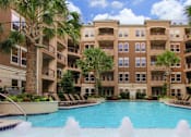 Thumbnail 1 of 36 - Luxury apartments with resort-style pool, palm trees, spacious sundeck with poolside lounge chairs, grilling station, fountains, and fitness center at Villa Piana Apartments in Dallas