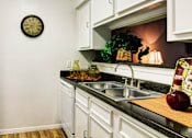Thumbnail 4 of 22 - Bright white kitchens with black countertops and wood plank floors at Waters of Winrock Apartments in Houston