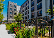 Thumbnail 12 of 12 - A metal fence with a decorative design separates a sidewalk from a grassy area.