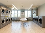 Thumbnail 5 of 12 - A laundromat with a row of washing machines and a table in the middle.