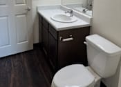 Thumbnail 7 of 14 - A white toilet sits in a bathroom next to a sink and mirror.
