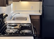 Thumbnail 14 of 14 - A kitchen with a black stove top oven and a black refrigerator.