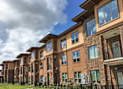 Thumbnail 3 of 11 - A row of brown brick apartment buildings with green shutters and balconies.
