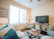 Thumbnail 6 of 11 - A living room with a white couch, a wooden coffee table, and a television on the wall.