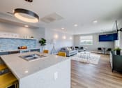 Thumbnail 5 of 32 - A modern kitchen with a large island and a living room with a couch and a TV.