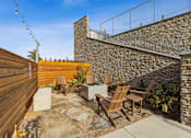 Thumbnail 13 of 27 - A patio with a stone wall and wooden chairs.