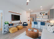Thumbnail 14 of 32 - A modern living room with a flat screen TV, a kitchen area, and a coffee table.
