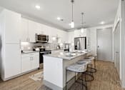 Thumbnail 8 of 27 - A modern kitchen with white cabinets and a central island.