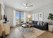 Thumbnail 6 of 27 - A living room with a grey couch, a coffee table, and a ceiling fan
