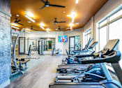 Thumbnail 14 of 27 - A gym with treadmills, exercise bikes, and a television at The Grand at Manor Apartments, Manor, Texas