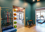 Thumbnail 13 of 27 - A gym with a row of exercise equipment including a treadmill, a rowing machine, and a stationary bike at The Grand at Manor Apartments, Texas