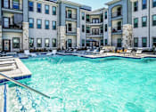 Thumbnail 9 of 27 - A swimming pool in front of a building with a deck and lounge chairs at The Grand at Manor Apartments, Manor, TX, 78653
