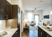 Thumbnail 4 of 27 - A modern kitchen with dark wood cabinets and a white countertop at The Grand at Manor Apartments, Texas 78653