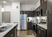 Thumbnail 3 of 27 - A modern kitchen with a stainless steel refrigerator and black cabinets at The Grand at Manor Apartments, Manor, TX