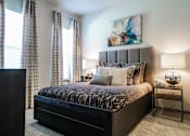 Thumbnail 5 of 27 - A bedroom with a large bed, a painting on the wall, and a window with curtains at The Grand at Manor Apartments, Manor, TX