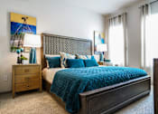 Thumbnail 6 of 27 - A bedroom with a bed, nightstand, and a painting on the wall at The Grand at Manor Apartments, Manor, 78653