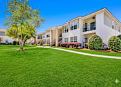 Thumbnail 3 of 23 - A tree stands in a grassy area in front of apartment buildings.