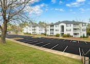 Thumbnail 5 of 19 - A parking lot in front of a white apartment building.