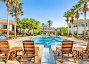 Thumbnail 13 of 23 - A pool surrounded by wooden chairs and palm trees.