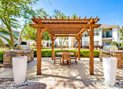 Thumbnail 14 of 23 - A wooden pergola with a bench and two pillars in front of a building.