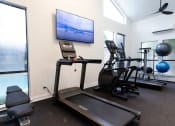 Thumbnail 34 of 47 - a gym with cardio equipment and a tv on the wall
