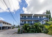 Thumbnail 2 of 23 - A white building with a blue roof is surrounded by greenery and power lines.