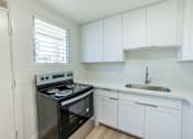 Thumbnail 9 of 23 - A kitchen with a stove, sink, and cabinets.