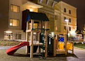 Thumbnail 3 of 5 - A playground with a red slide and a yellow and blue climbing structure.