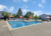 Thumbnail 2 of 21 - A large outdoor swimming pool with red umbrellas and a slide.