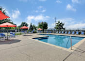 Thumbnail 3 of 21 - A pool area with red umbrellas and blue chairs.