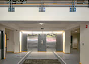 Thumbnail 12 of 25 - A hallway with two elevators and a fire extinguisher on the wall.