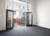 Thumbnail 20 of 25 - A room with a carpeted floor and a view of a building through the glass doors.